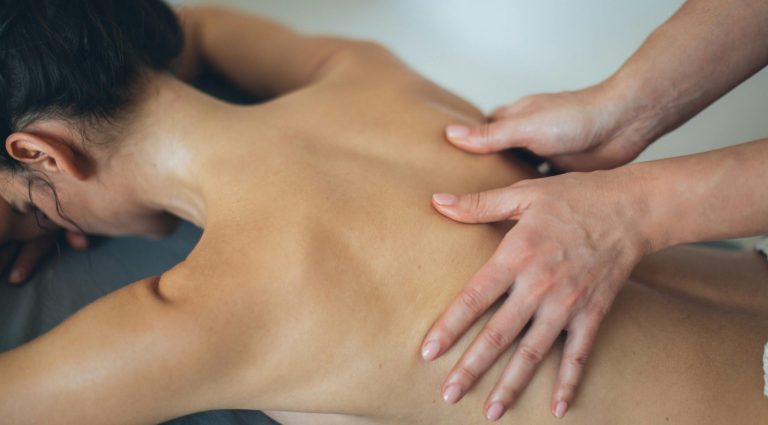 Triggerpunktmassage Dunkelhaarige Frau liegt auf der Massageliege. Masseurin drückt bewusst auf die Triggerpunkte am Rücken.